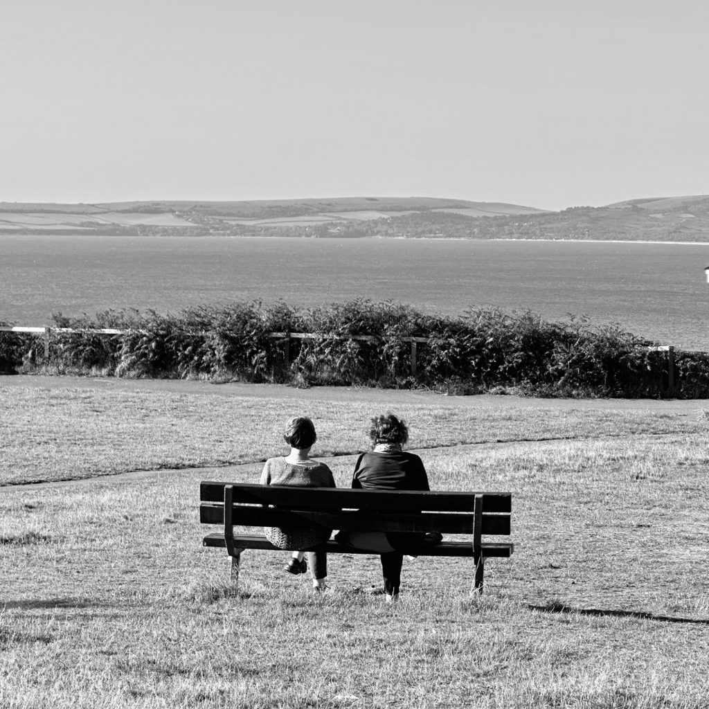 Two people sitting in a bench looking at the sea
